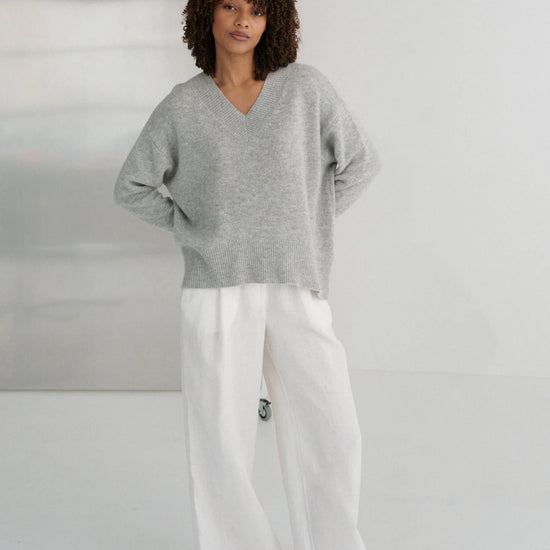 Person wearing a gray sweater and white pants against a plain background