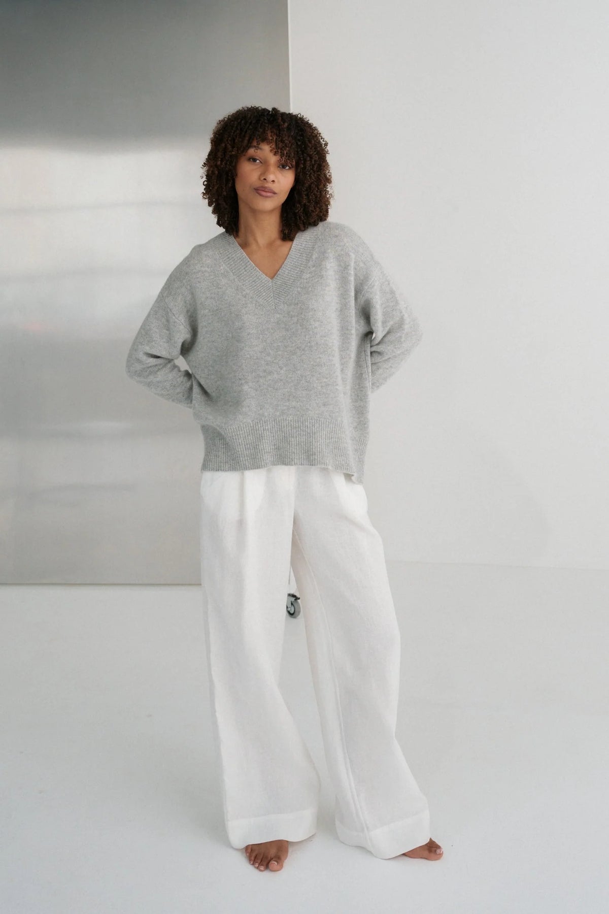 Person wearing a gray sweater and white pants against a plain background