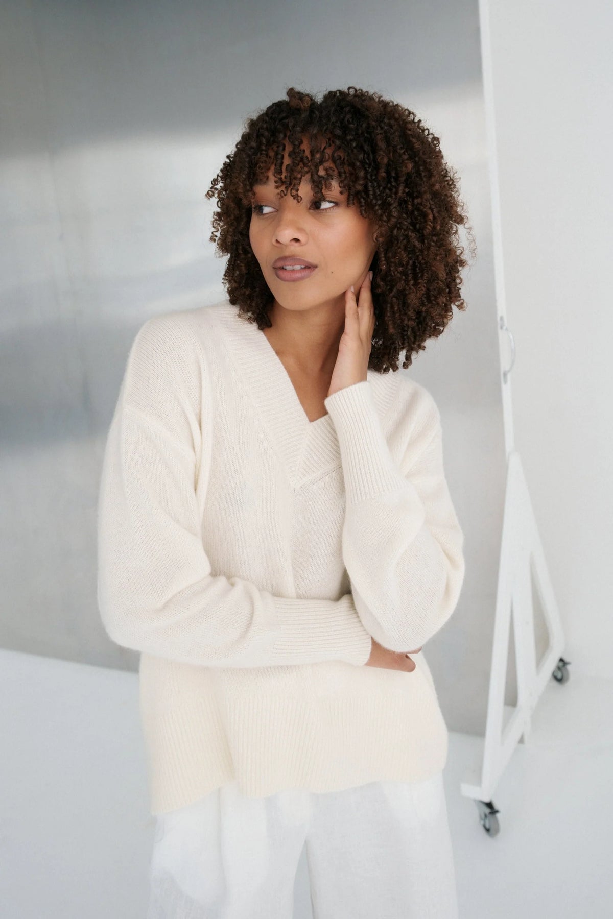 Woman wearing a cream sweater and white pants against a plain background