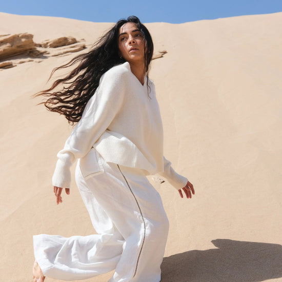 Woman in a white outfit standing on sand dunes with a clear blue sky.
