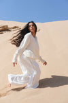 Woman in a white outfit standing on sand dunes with a clear blue sky.