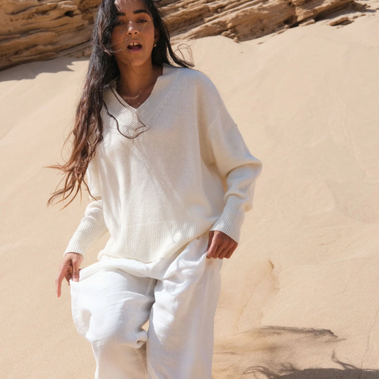 Person wearing a white outfit standing in a desert landscape with sand dunes and rocks.