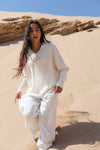 Person wearing a white outfit standing in a desert landscape with sand dunes and rocks.