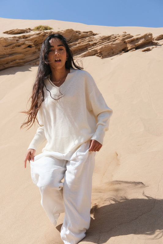 Person wearing a white outfit standing in a desert landscape with sand dunes and rocks.