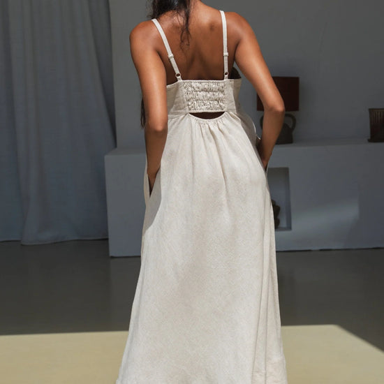 Woman wearing a beige linen dress standing in a minimalistic room.