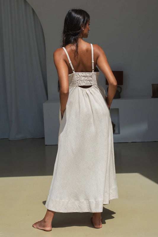 Woman wearing a beige linen dress standing in a minimalistic room.