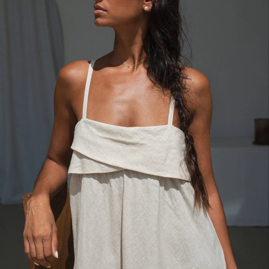 Woman wearing a light-colored linen dress with a plain background
