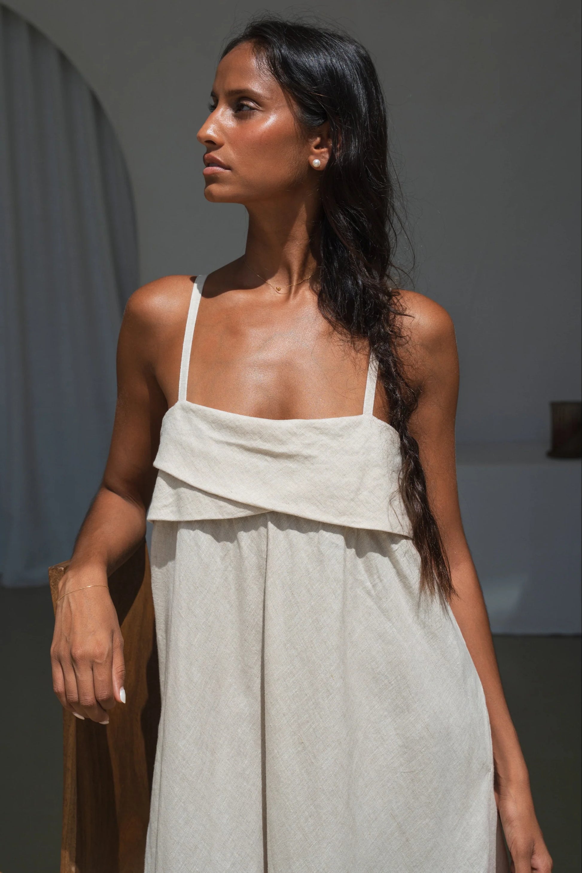 Woman wearing a light-colored linen dress with a plain background