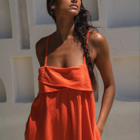 Woman wearing an orange linen dress standing against a white wall with arches.