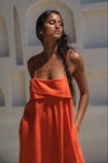 Woman wearing an orange linen dress standing against a white wall with arches.