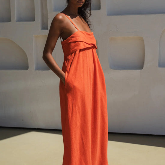 Woman wearing an orange linen dress standing against a white wall with geometric shapes.