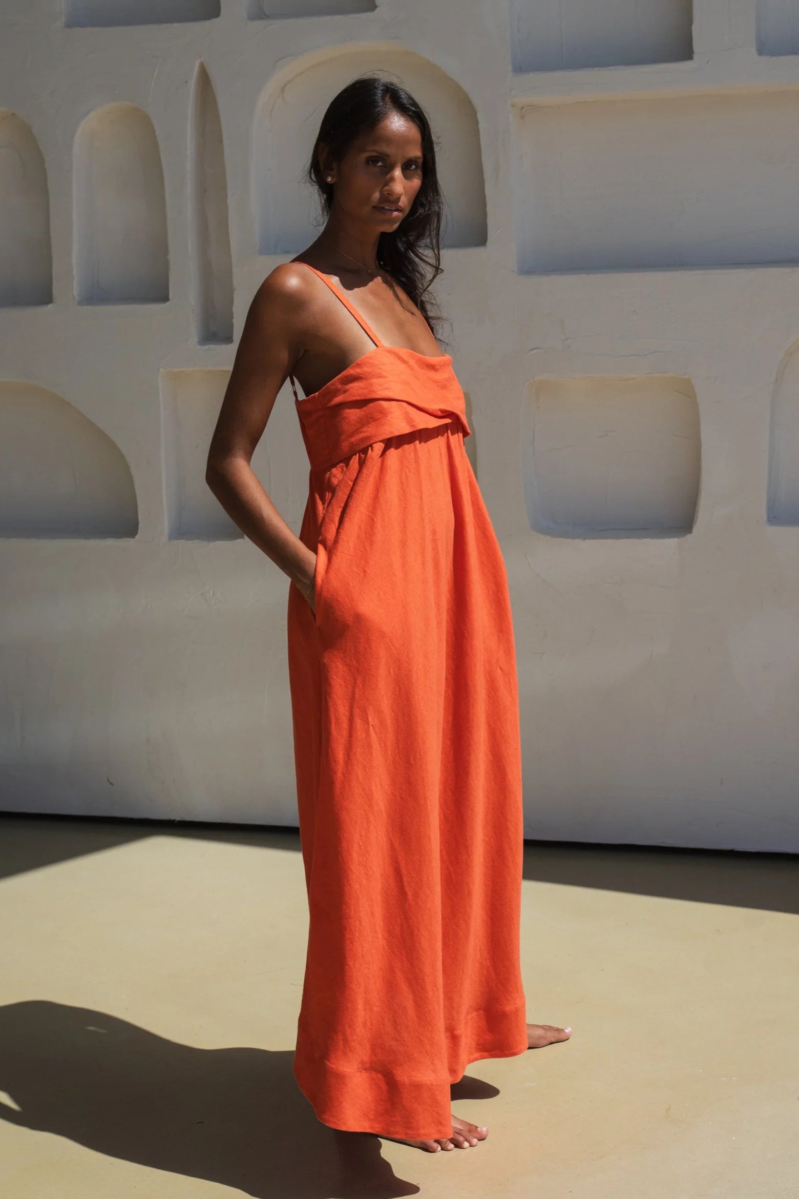 Woman wearing an orange linen dress standing against a white wall with geometric shapes.