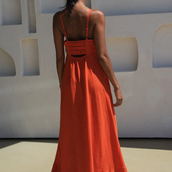 Woman in an orange linen dress standing against a white wall with geometric shapes.