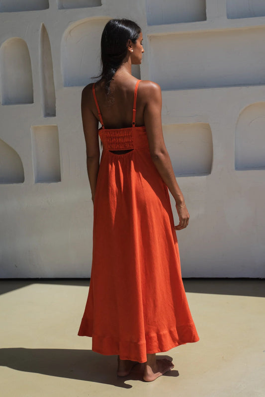Woman in an orange linen dress standing against a white wall with geometric shapes.