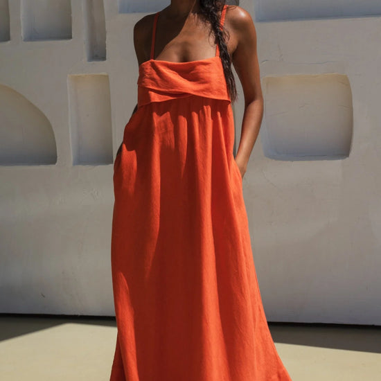 Woman wearing an orange linen dress standing against a white wall with arched windows.
