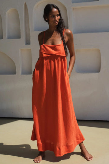 Woman wearing an orange linen dress standing against a white wall with arched windows.
