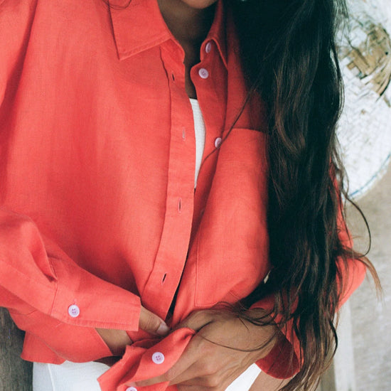 Woman wearing a coral shirt and white shorts outdoors from lilly pilly