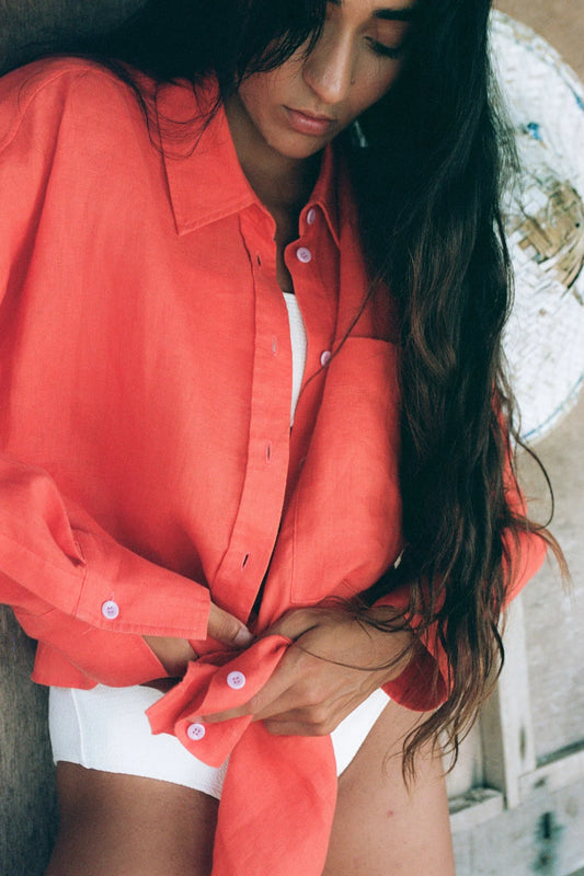 Woman wearing a coral shirt and white shorts outdoors from lilly pilly