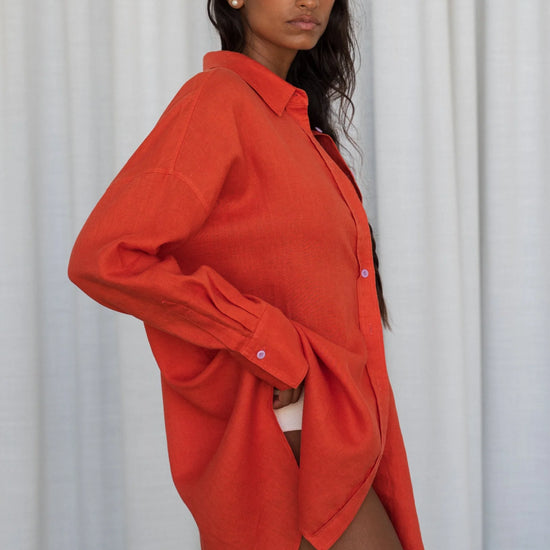 Woman wearing an orange oversized shirt from lilly pilly against a white curtain background