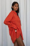 Woman wearing an orange oversized shirt from lilly pilly against a white curtain background