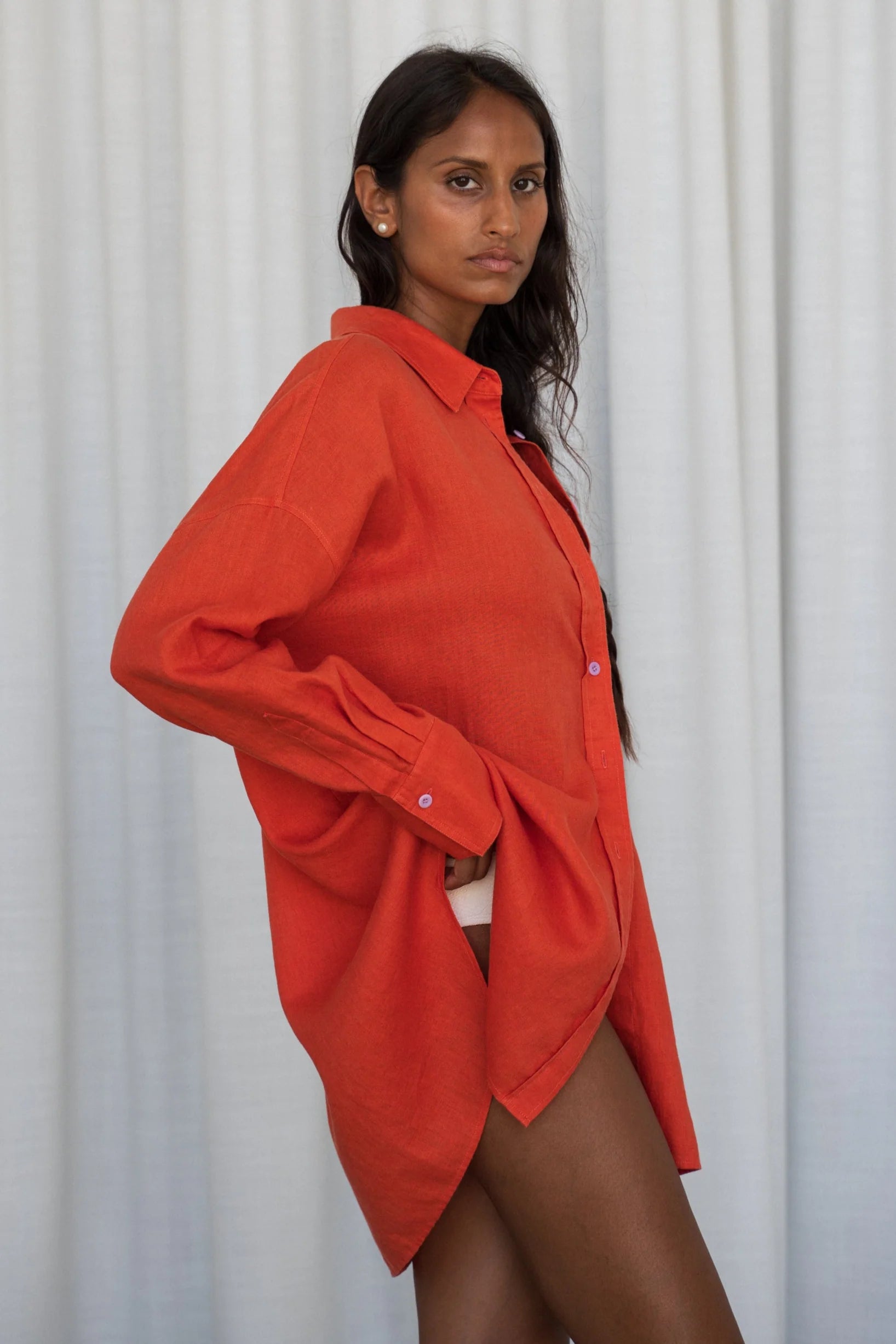 Woman wearing an orange oversized shirt from lilly pilly against a white curtain background