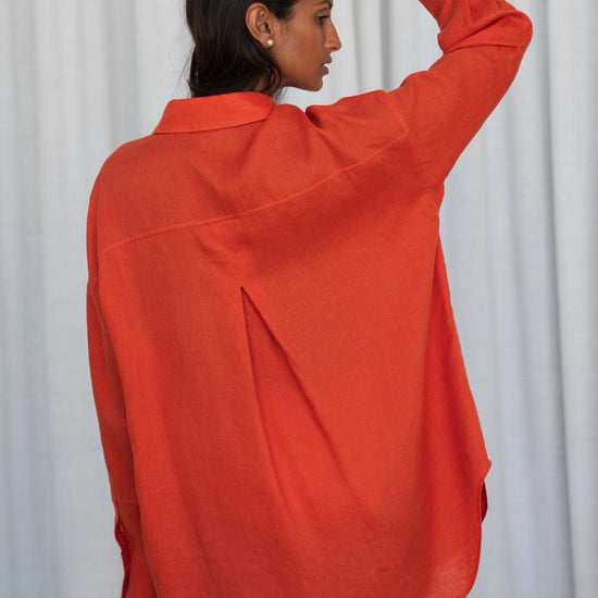 Person wearing an orange shirt from lilly pilly against a white curtain backgroundi