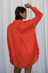 Person wearing an orange shirt from lilly pilly against a white curtain backgroundi