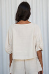 Person wearing a beige outfit against a white curtain background rear view from Lilly Pilly