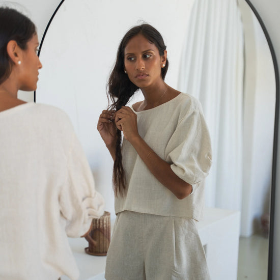 Woman adjusting her hair in front of a mirror wearing a light-colored outfit from Lilly Pilly