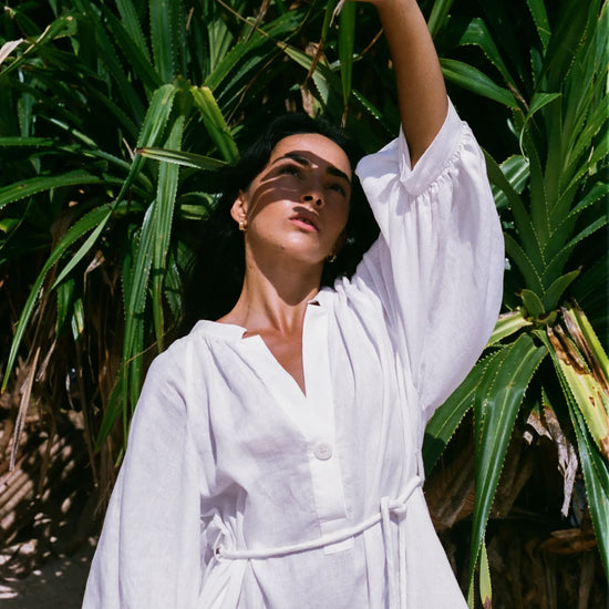 Woman in a white linen dress standing among tropical plants