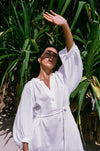 Woman in a white linen dress standing among tropical plants