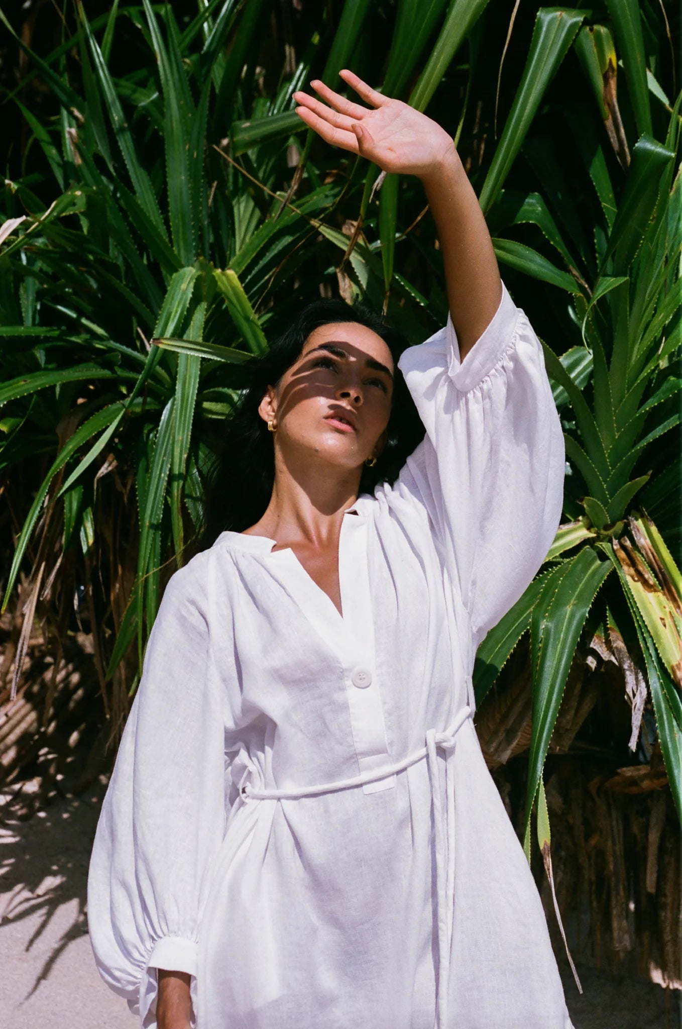 Woman in a white linen dress standing among tropical plants