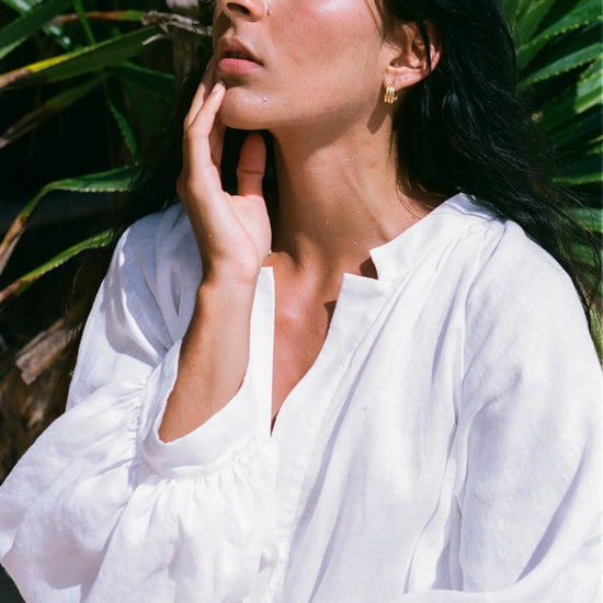 Woman in a white dress standing against a green leafy background