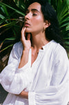Woman in a white dress standing against a green leafy background