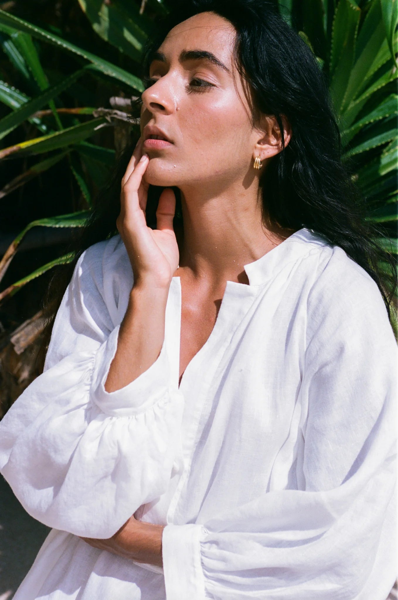 Woman in a white dress standing against a green leafy background