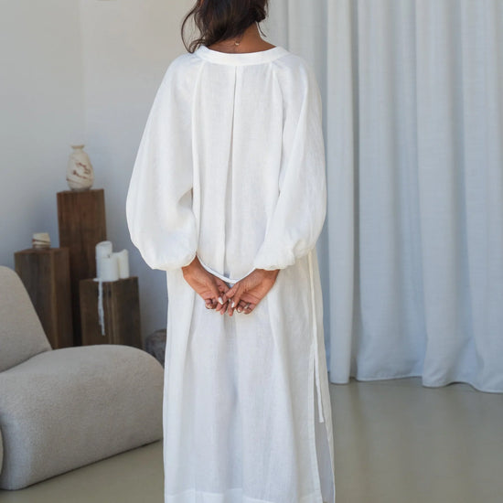 Woman wearing a white dress standing in a minimalistic room with neutral colors.