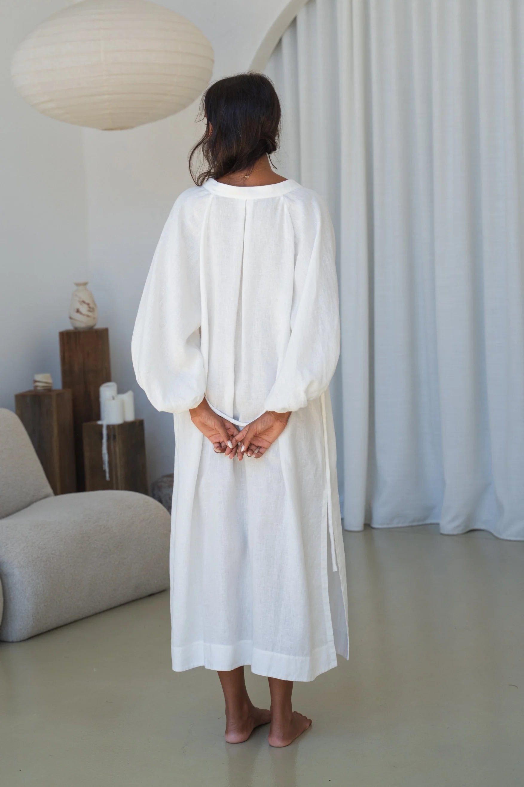 Woman wearing a white dress standing in a minimalistic room with neutral colors.