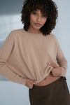 Woman wearing a beige sweater and brown pants against a neutral background