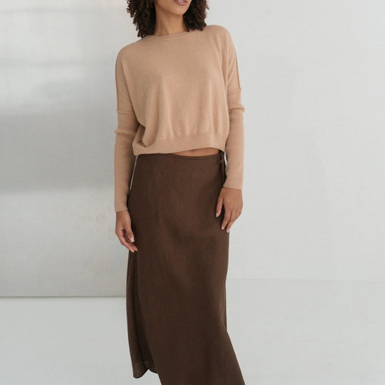 Woman wearing a beige sweater and brown skirt against a white background