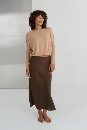 Woman wearing a beige sweater and brown skirt against a white background