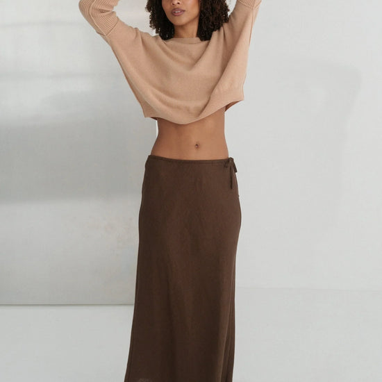 Woman wearing a beige top and brown skirt against a white background