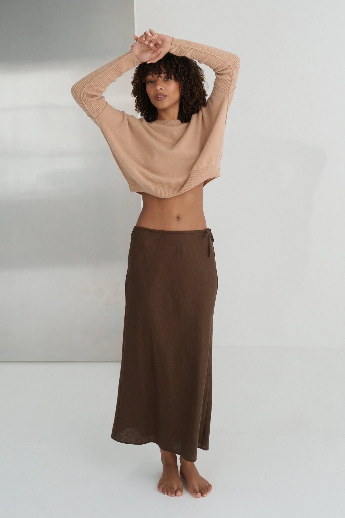 Woman wearing a beige top and brown skirt against a white background