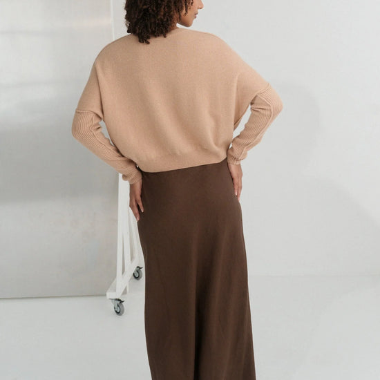 Person wearing a beige sweater and brown skirt standing against a white background