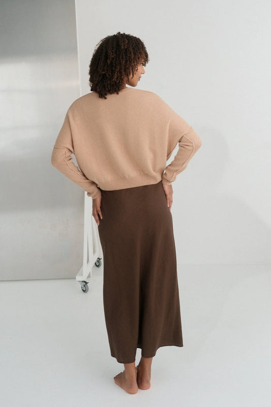 Person wearing a beige sweater and brown skirt standing against a white background