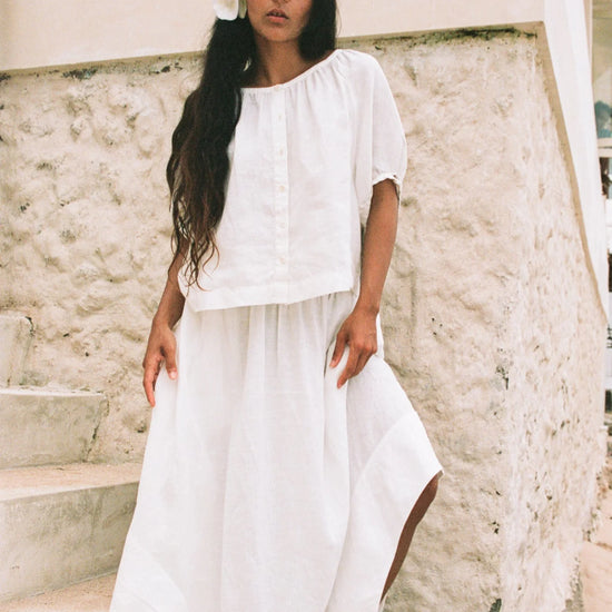 Woman in a white outfit standing on stone steps with a neutral background
