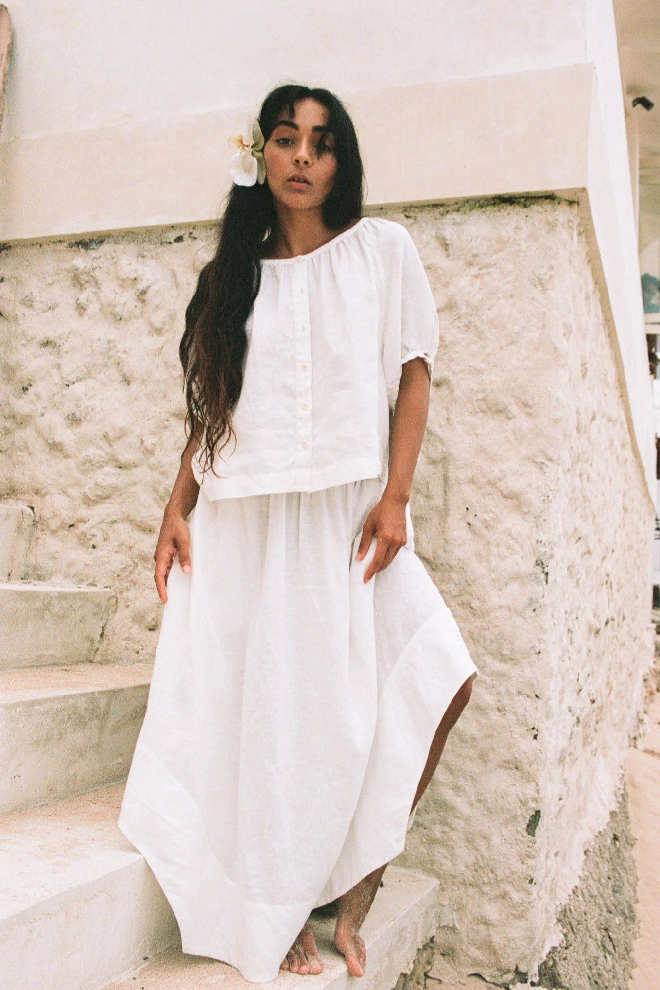 Woman in a white outfit standing on stone steps with a neutral background
