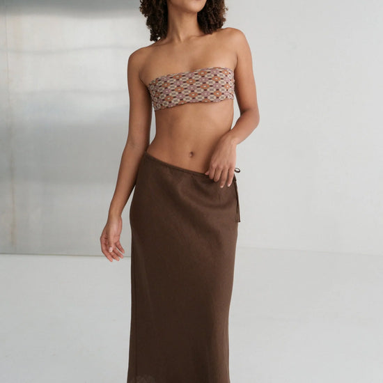 Woman wearing a strapless top and brown skirt against a neutral background