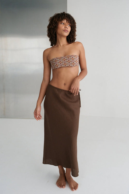 Woman wearing a strapless top and brown skirt against a neutral background