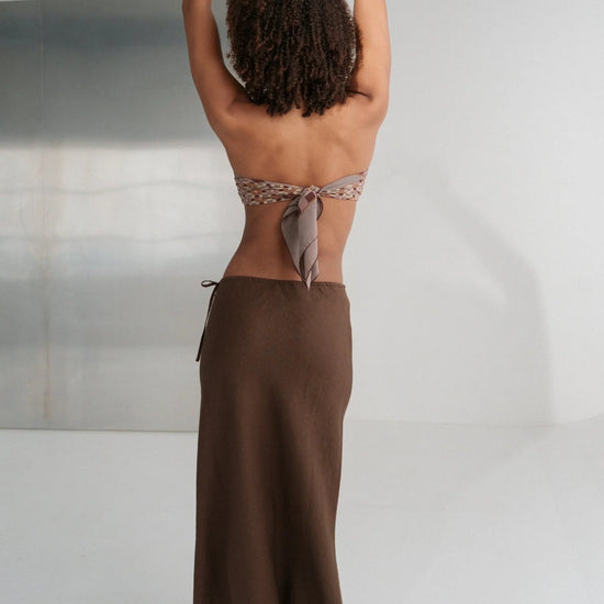 Person wearing a brown skirt and topless top against a neutral background