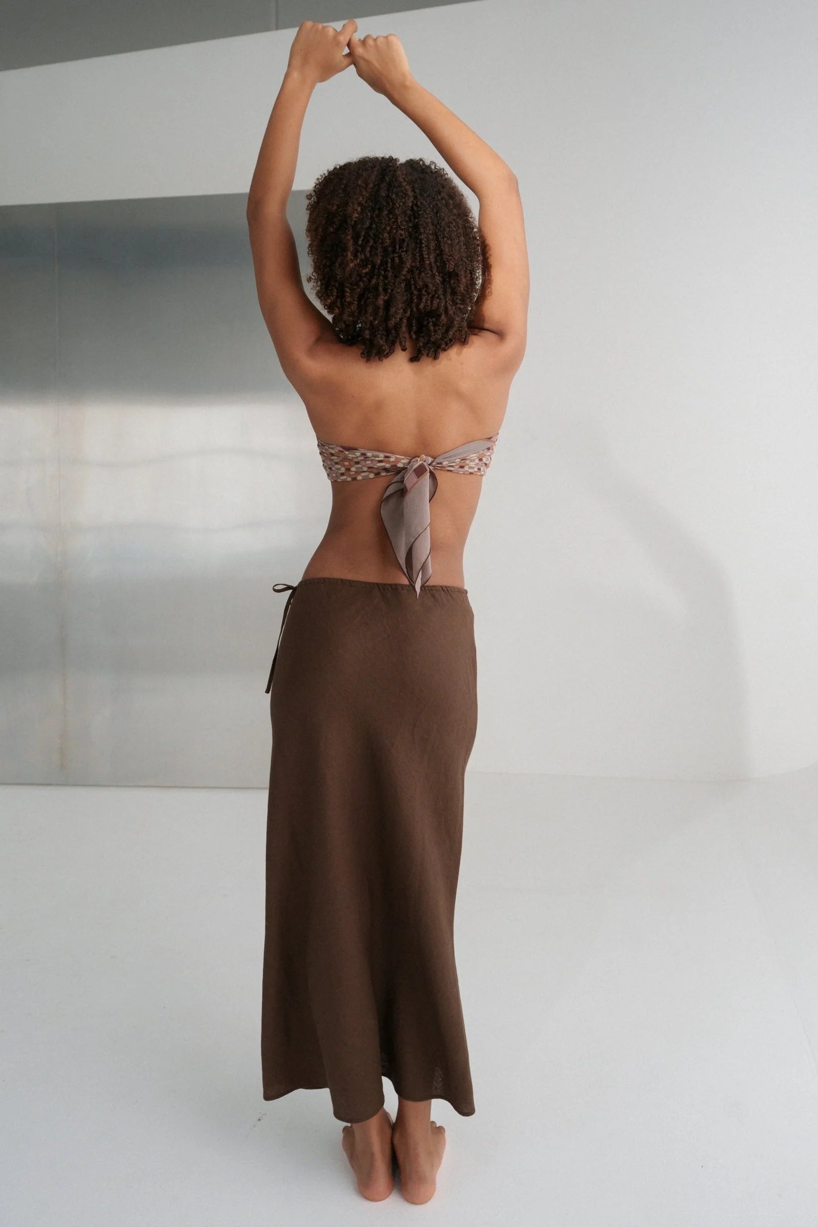 Person wearing a brown skirt and topless top against a neutral background